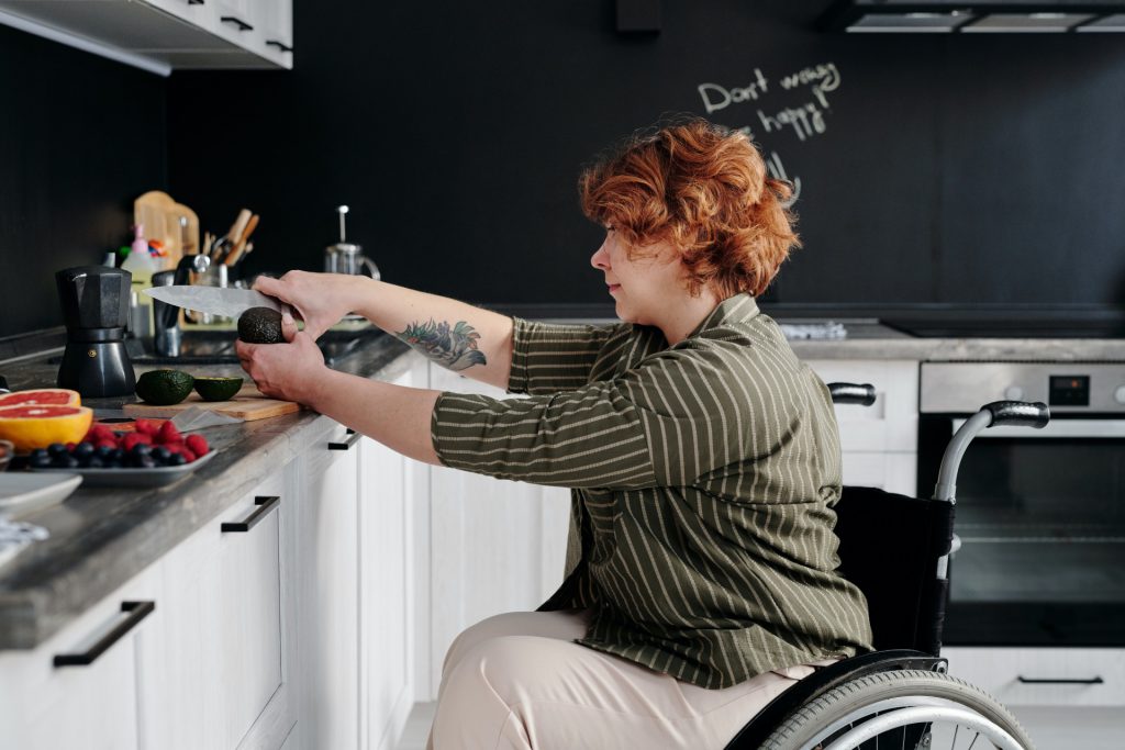 Kobieta na wózku inwalidzkim w kuchni przyżądza jedzenie